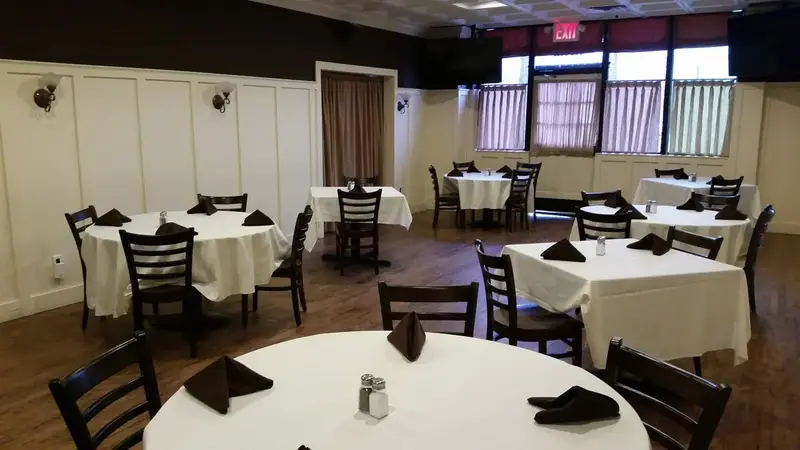 The private party room with round tables set with white cloths and dark napkins on a wood floor