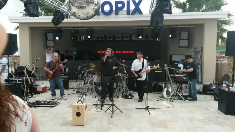 Victims of Rock performing in daylight on an outdoor patio stage with a white tiled floor